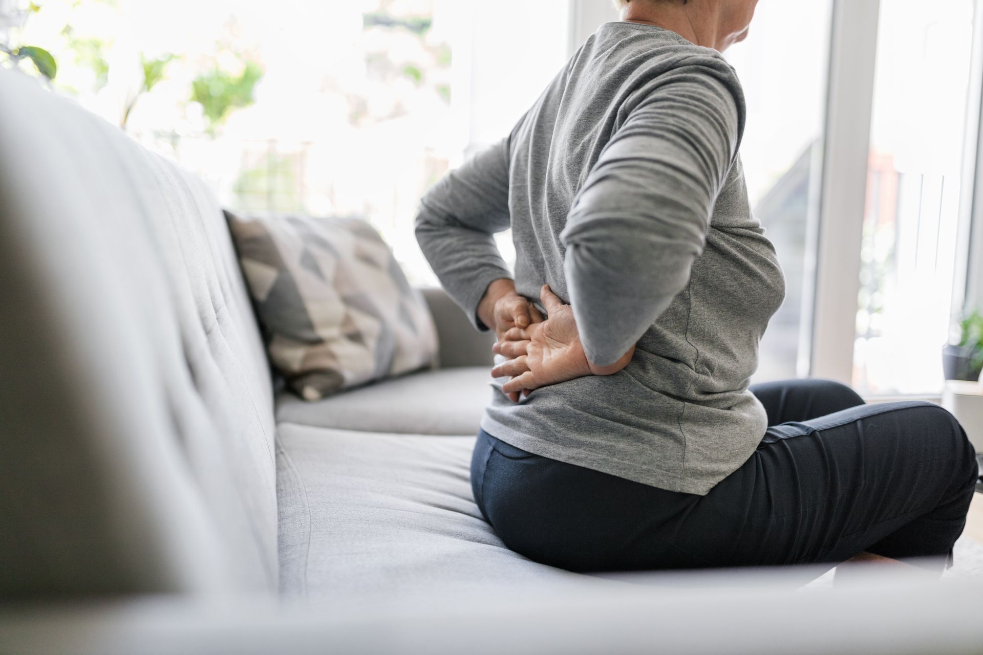 Person sitting on a couch, holding their lower back in pain.