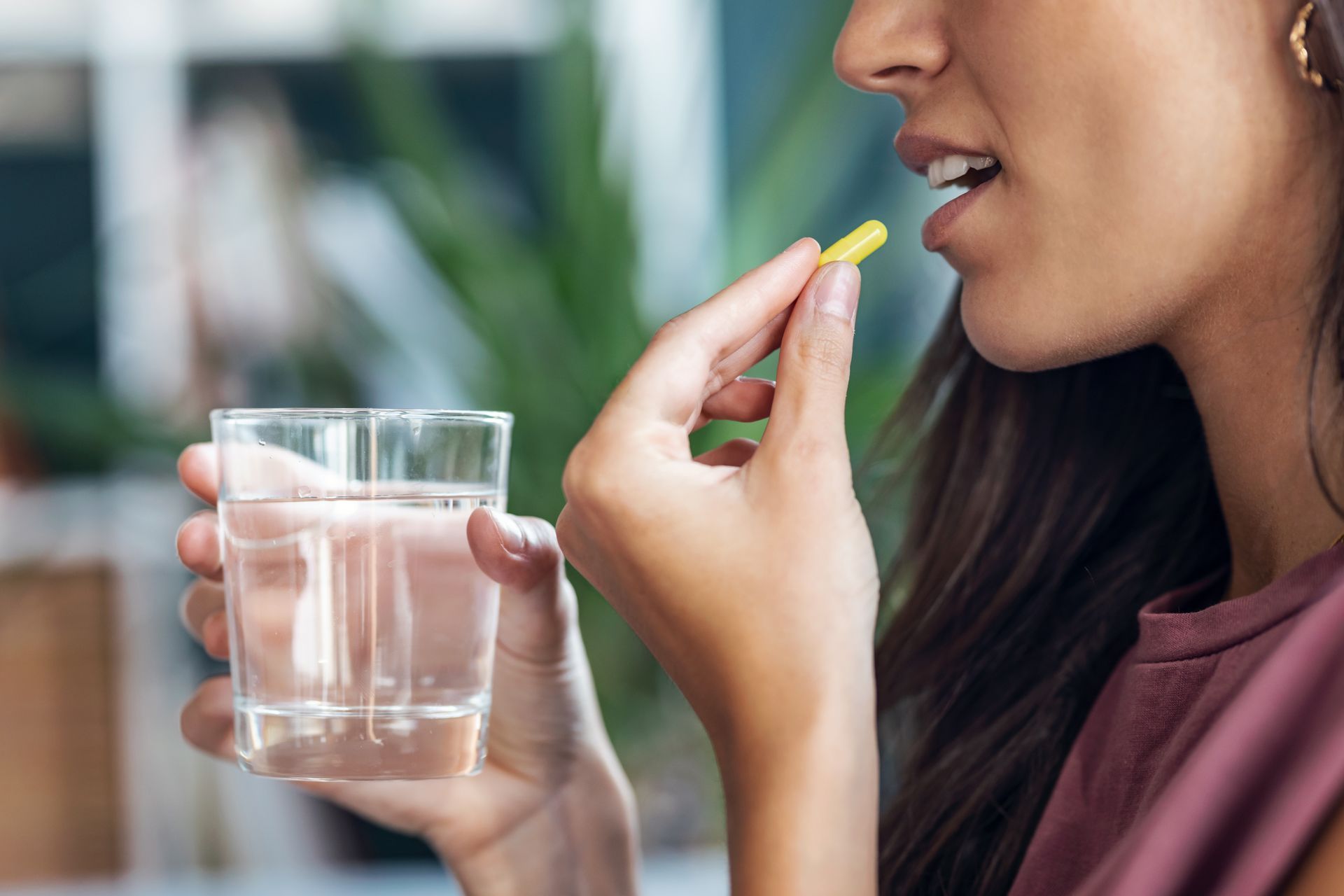 Woman holding a glass of water and a yellow pill near her mouth indoors