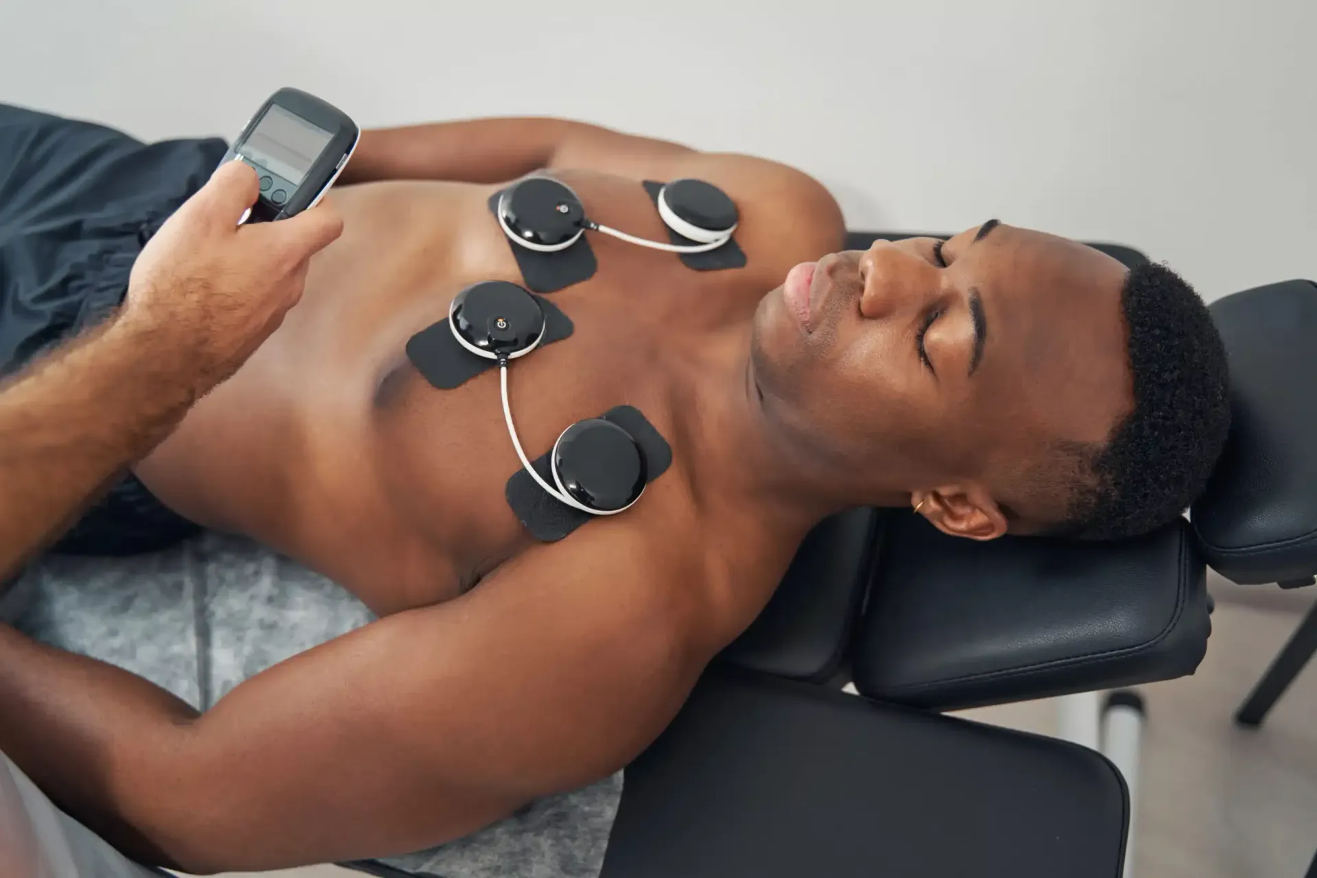 Man lying on a treatment table with electrodes on chest while a clinician holds a device nearby