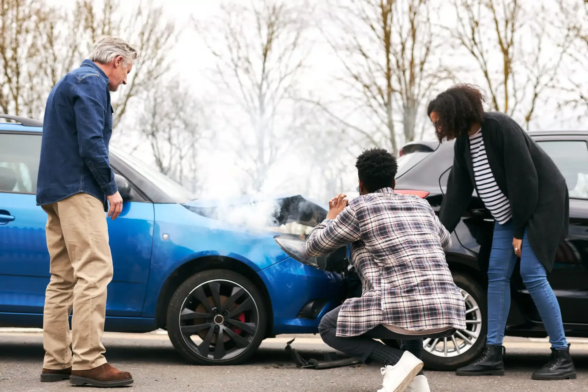 Three people inspecting damage on the front of a blue car after a collision
