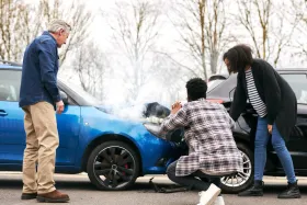 Three people inspecting damage on the front of a blue car after a crash