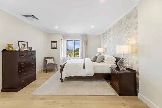 Bright bedroom with a bed, dresser, nightstands, patterned wallpaper, and a window with curtains