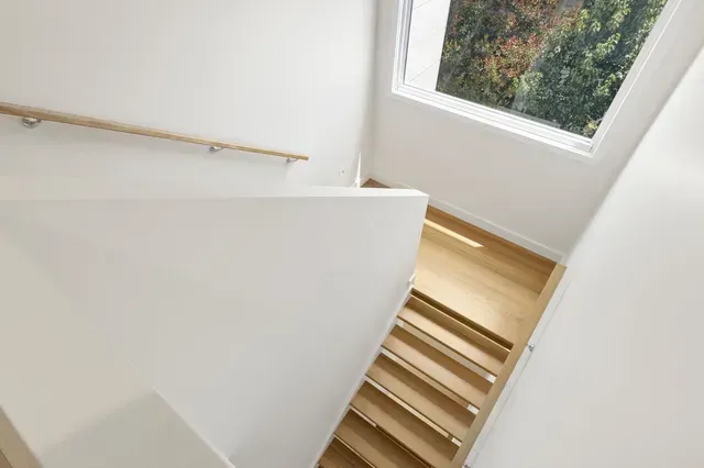White stairwell with wooden steps and a large window letting in natural light