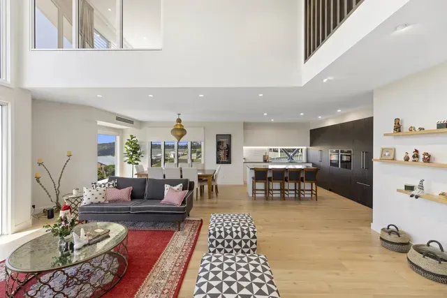 Bright modern living room with sofa, patterned ottomans, glass table, and open kitchen with island