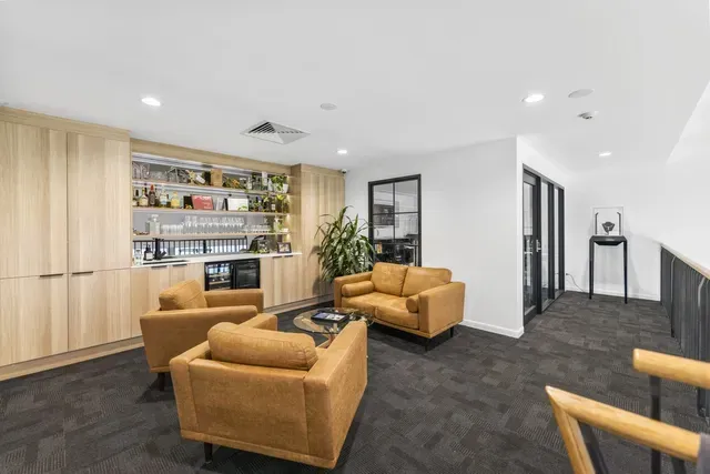 Modern office lounge with tan armchairs, wooden shelving, and a dark carpeted floor