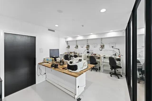 Bright lab workspace with workbench, microscopes, computers, and large black door.