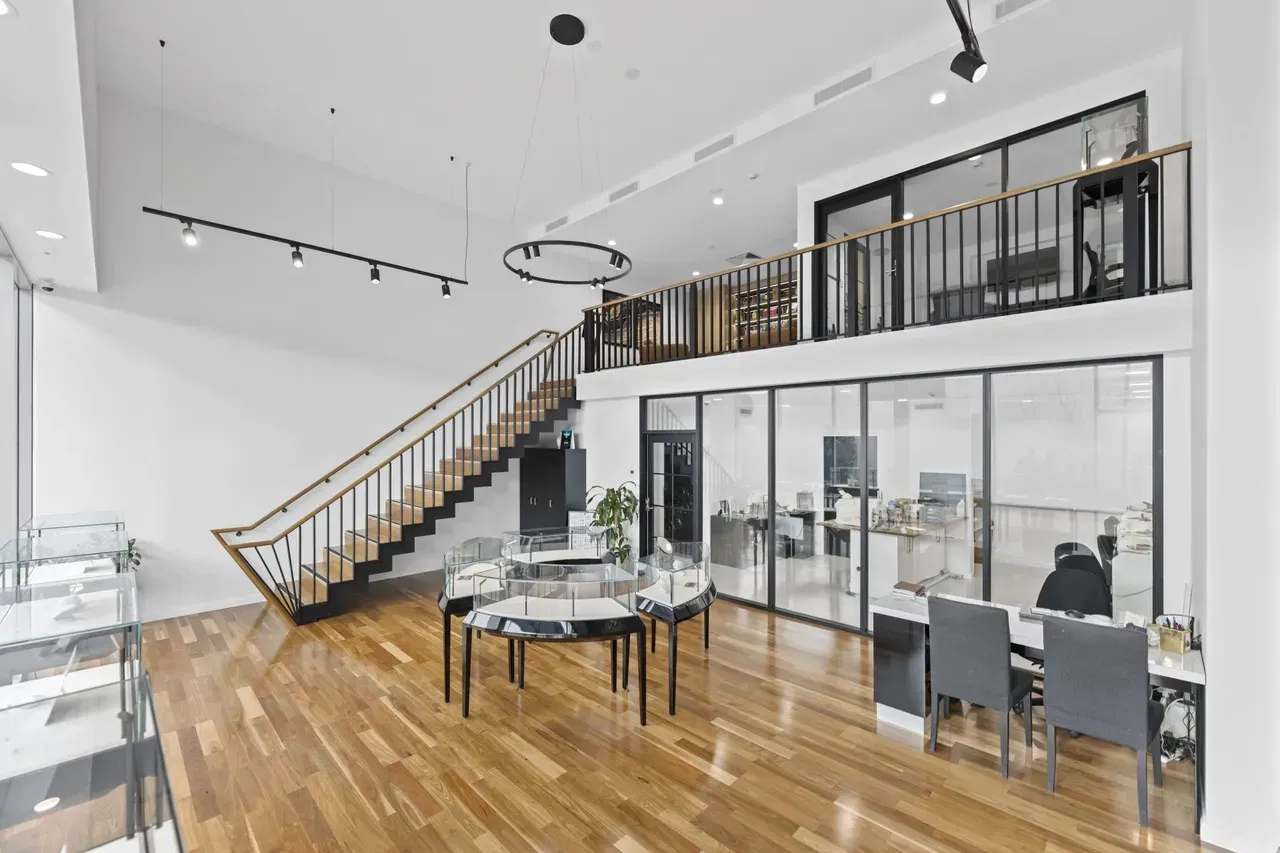 Modern open loft with hardwood floors, glass walls, staircase, and a dining table under track lighting