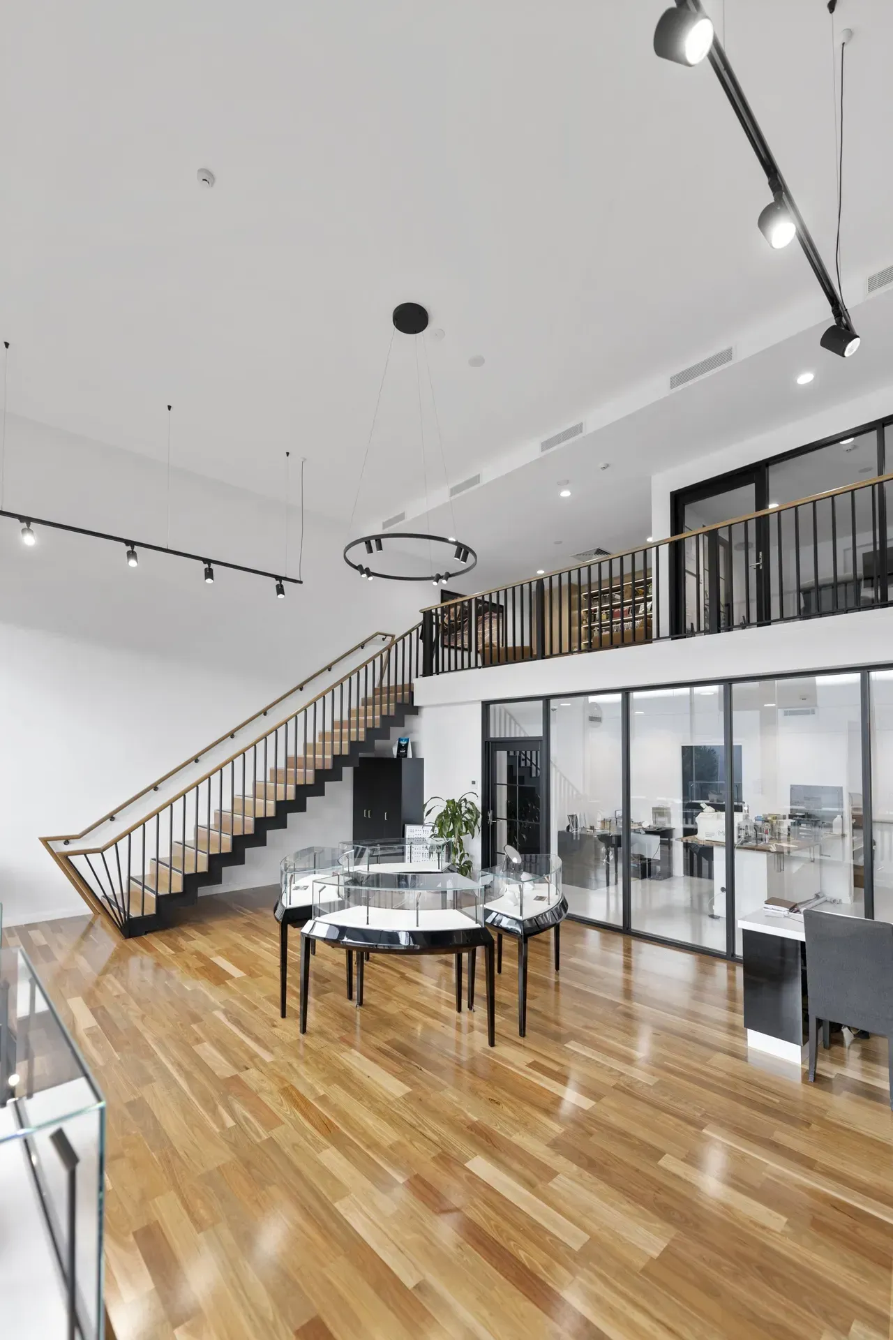 Bright modern loft interior with wood floors, staircase, dining table, and glass-walled upper level.