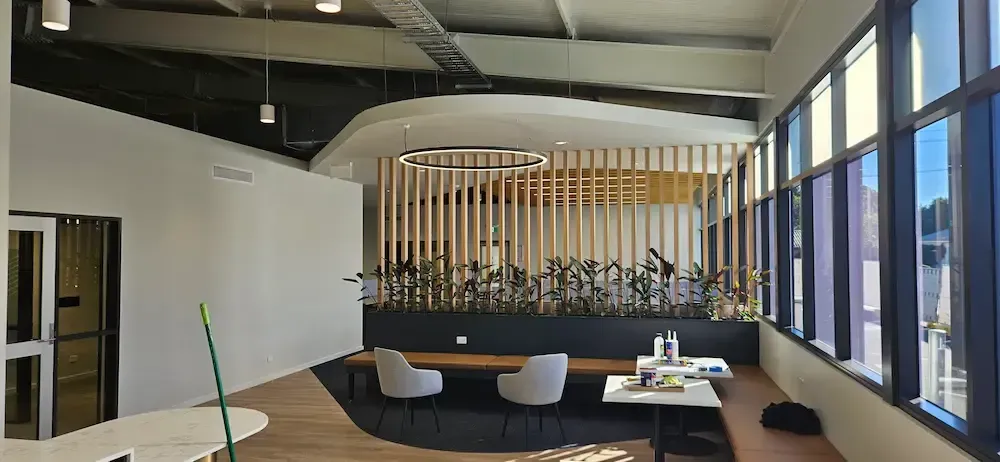 Modern lounge with black couches, white chairs, wood slat divider, and floor-to-ceiling windows