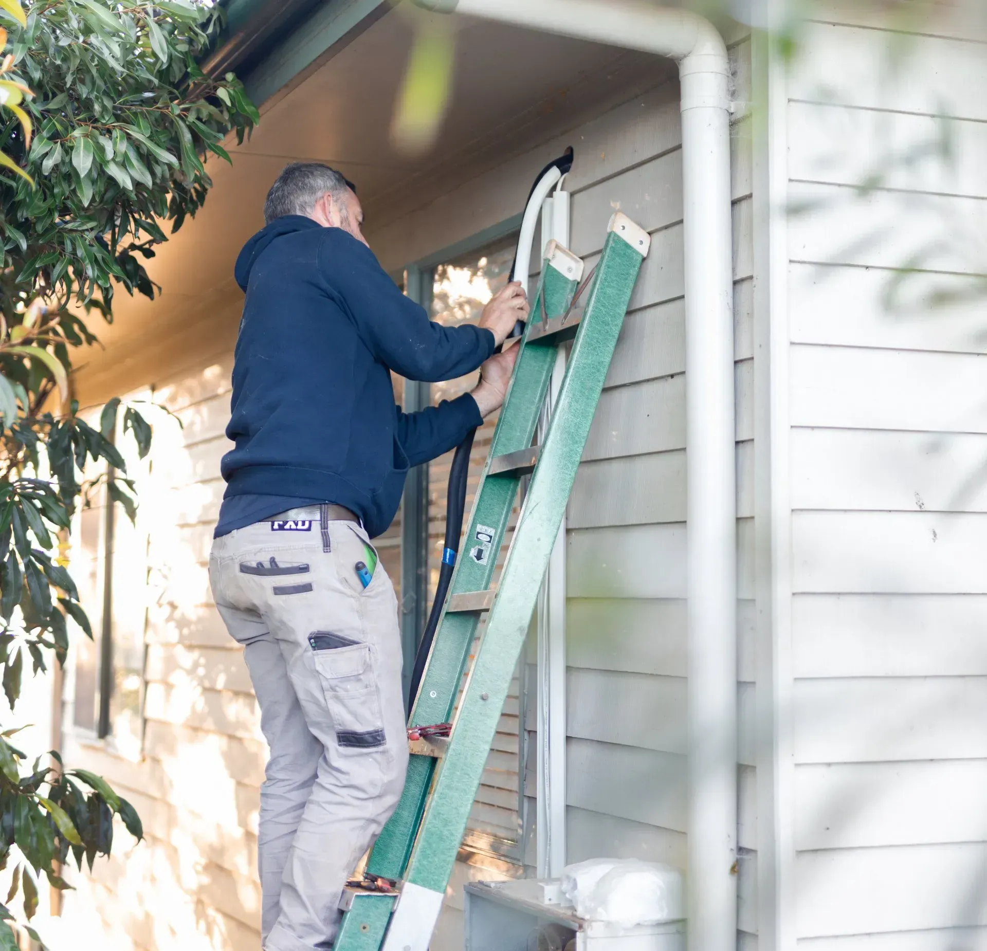 Worker on a ladder repairing the exterior of a house near a downspout.