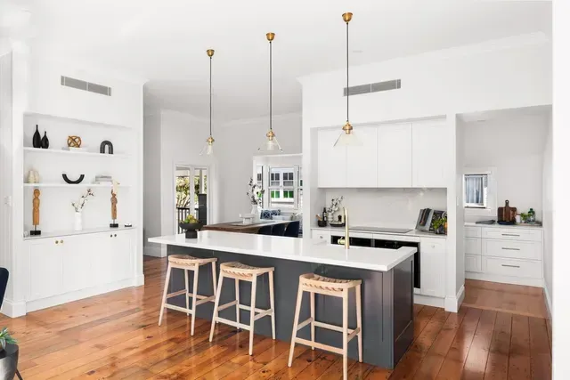 Bright modern kitchen with white cabinets, black island, wood floors, and two stools