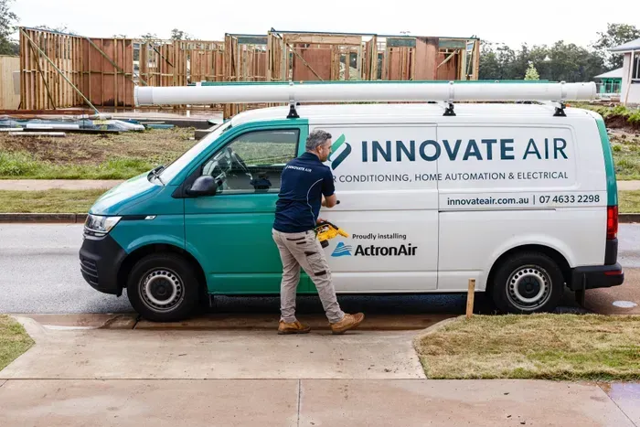 Worker servicing a white Innovate Air van parked outside a house under construction