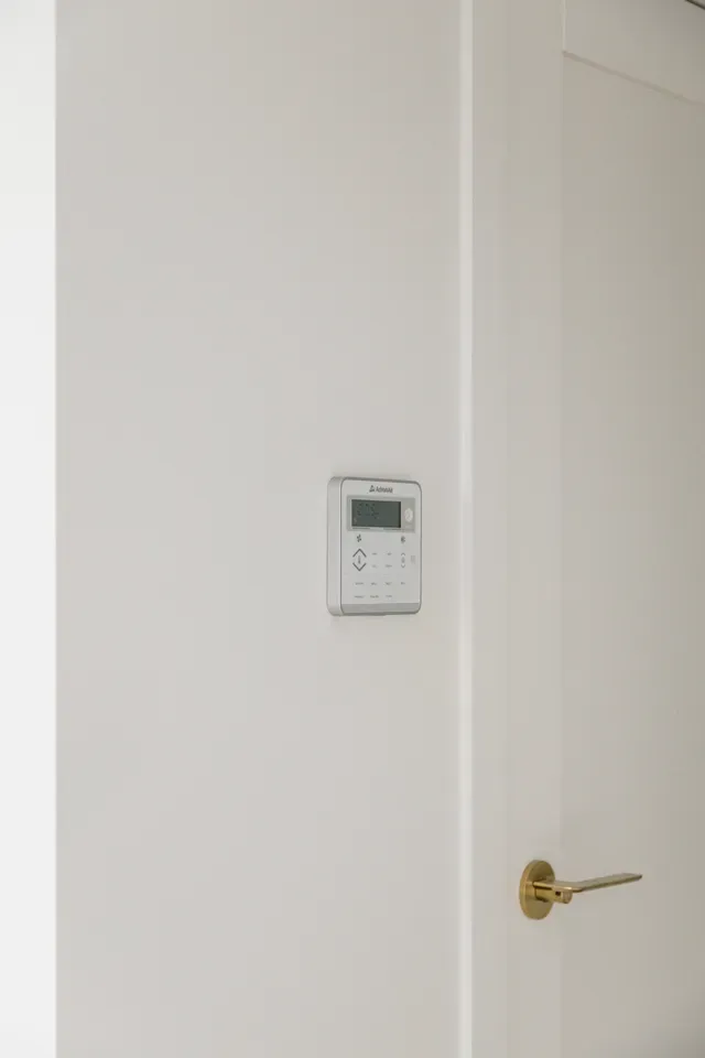 White hallway with a closed door, brass handle, and a small wall-mounted control panel.