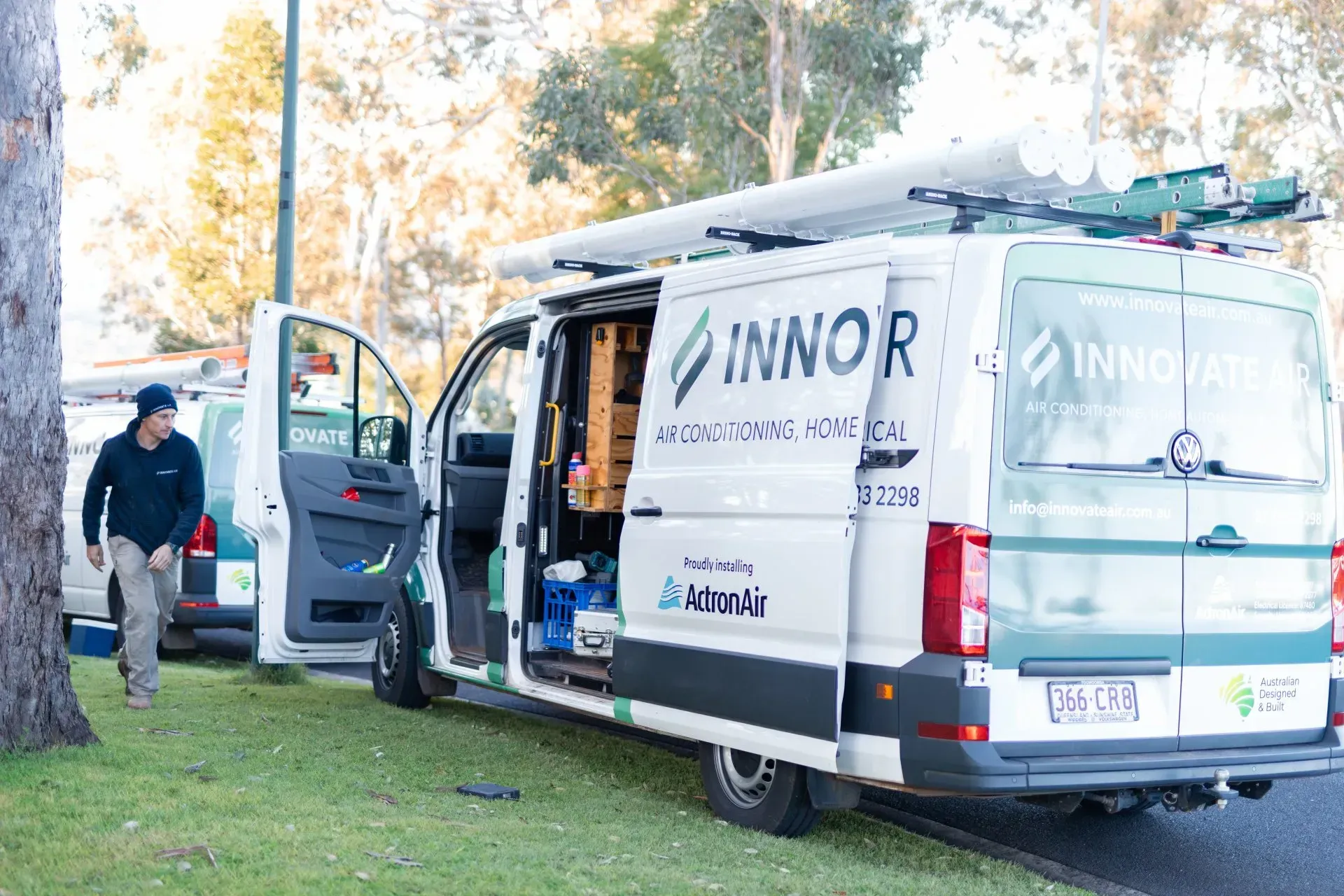 People unloading equipment from a white Innovor van parked on grass near trees