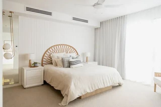 Bright minimalist bedroom with a rattan headboard, white bedding, and sheer curtains