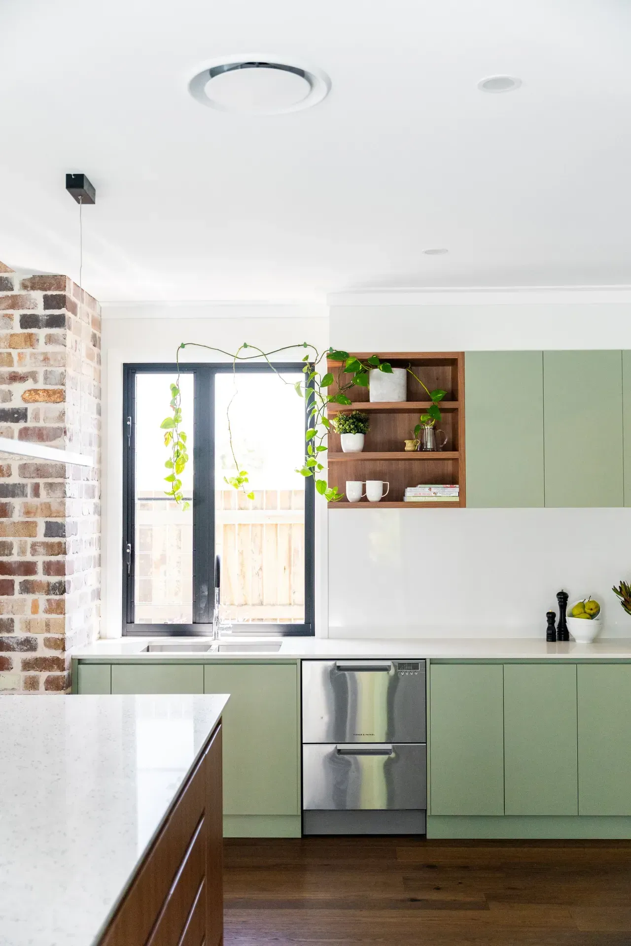 Bright modern kitchen with green cabinets, brick wall, and a window over the sink.