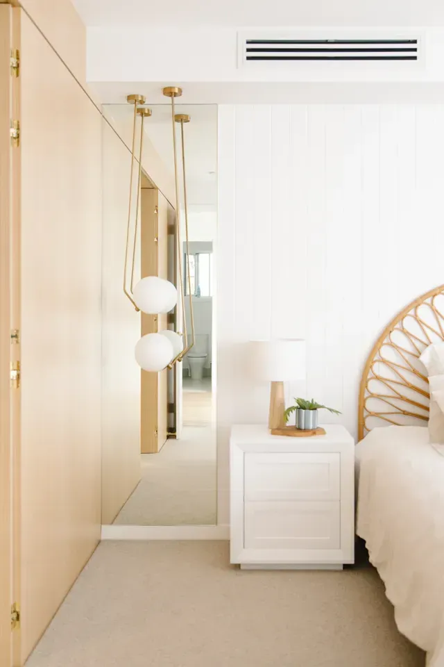 Bright minimalist bedroom with mirrored wardrobe, white nightstand, and rattan bed frame in neutral tones