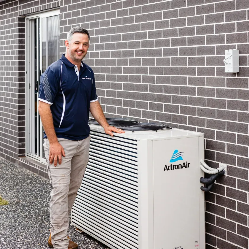 Technician standing beside an outdoor air-conditioning unit against a brick wall