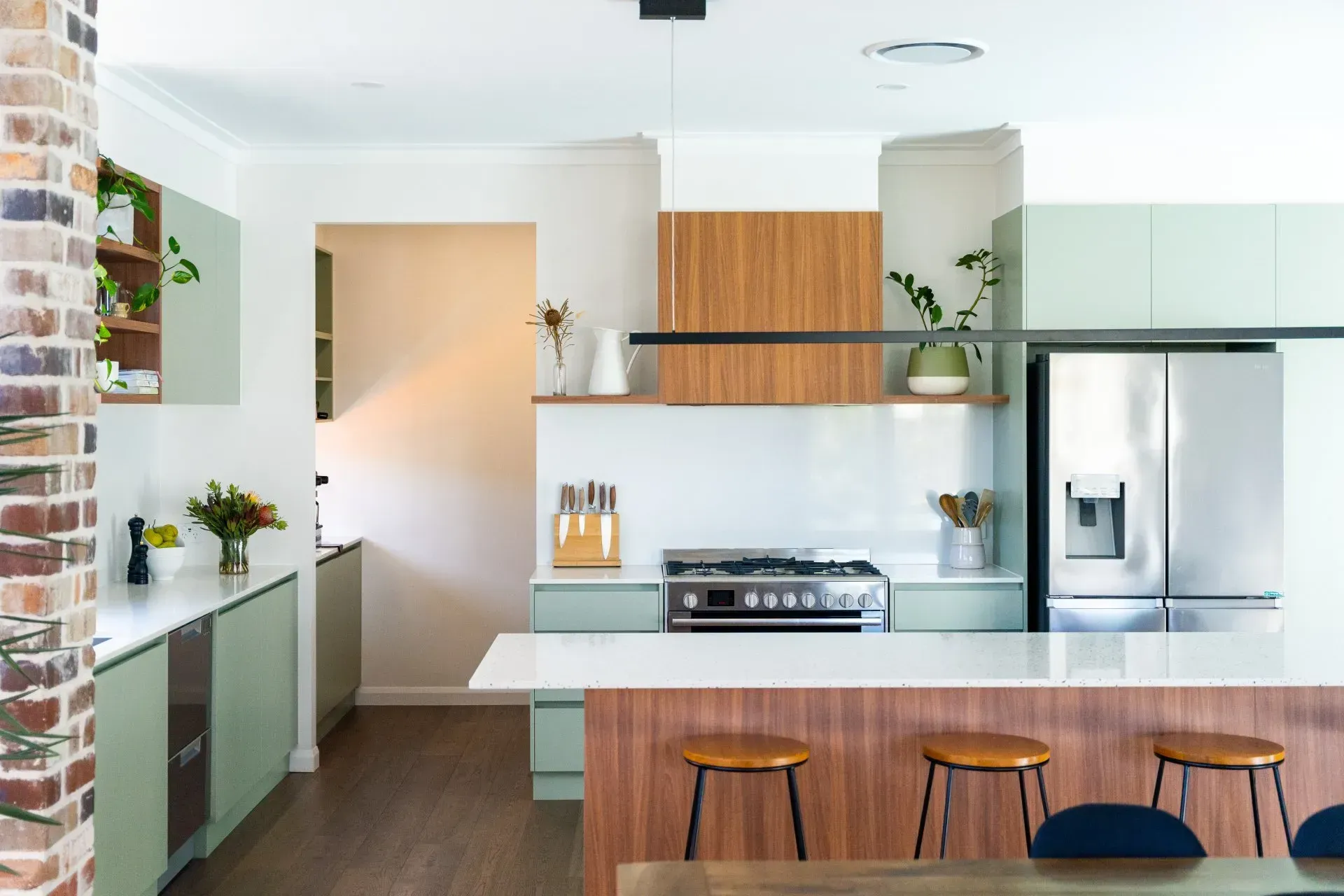 Modern kitchen with island, stainless steel appliances, wood stools, and white cabinetry