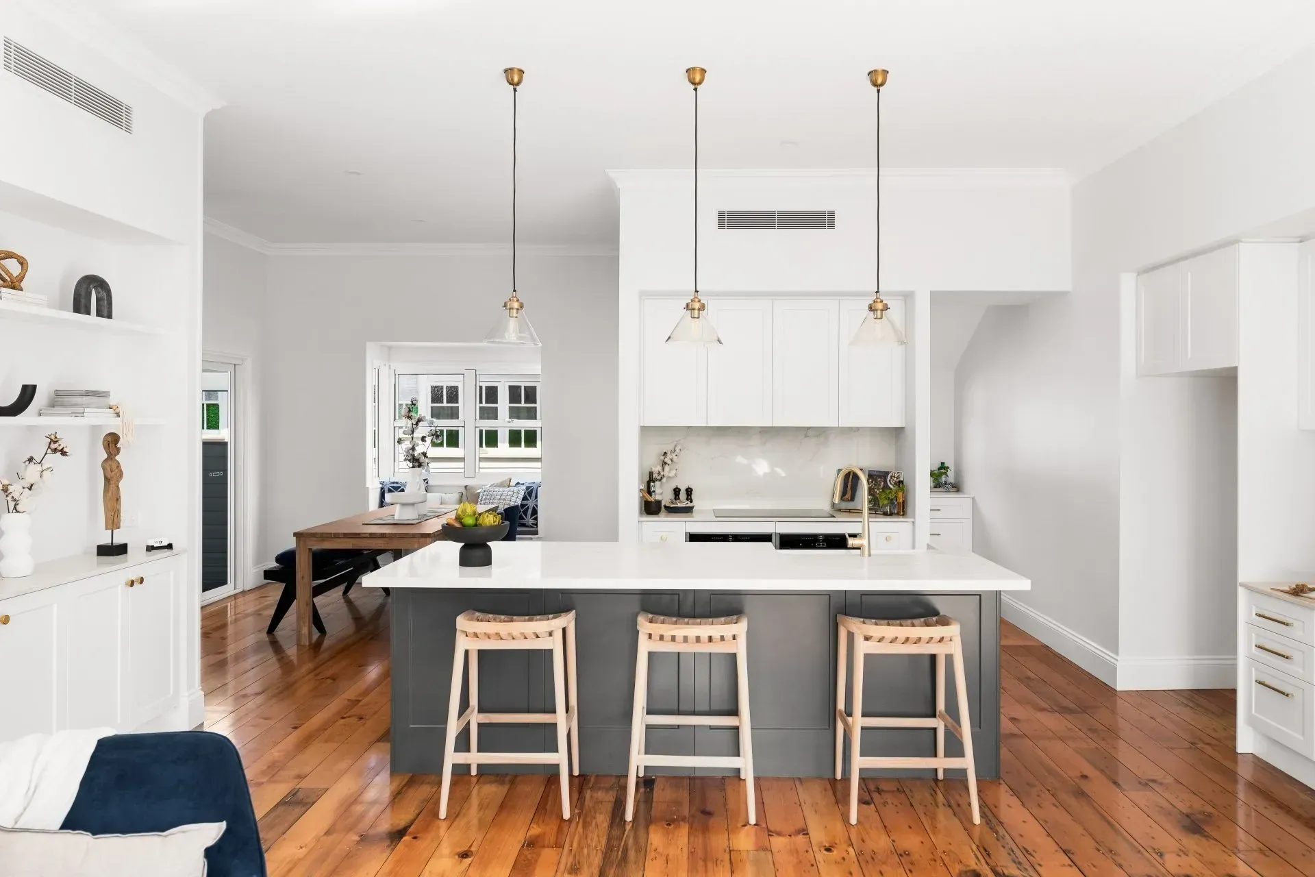 Bright modern kitchen with a large island, three stools, white cabinets, and hardwood floors