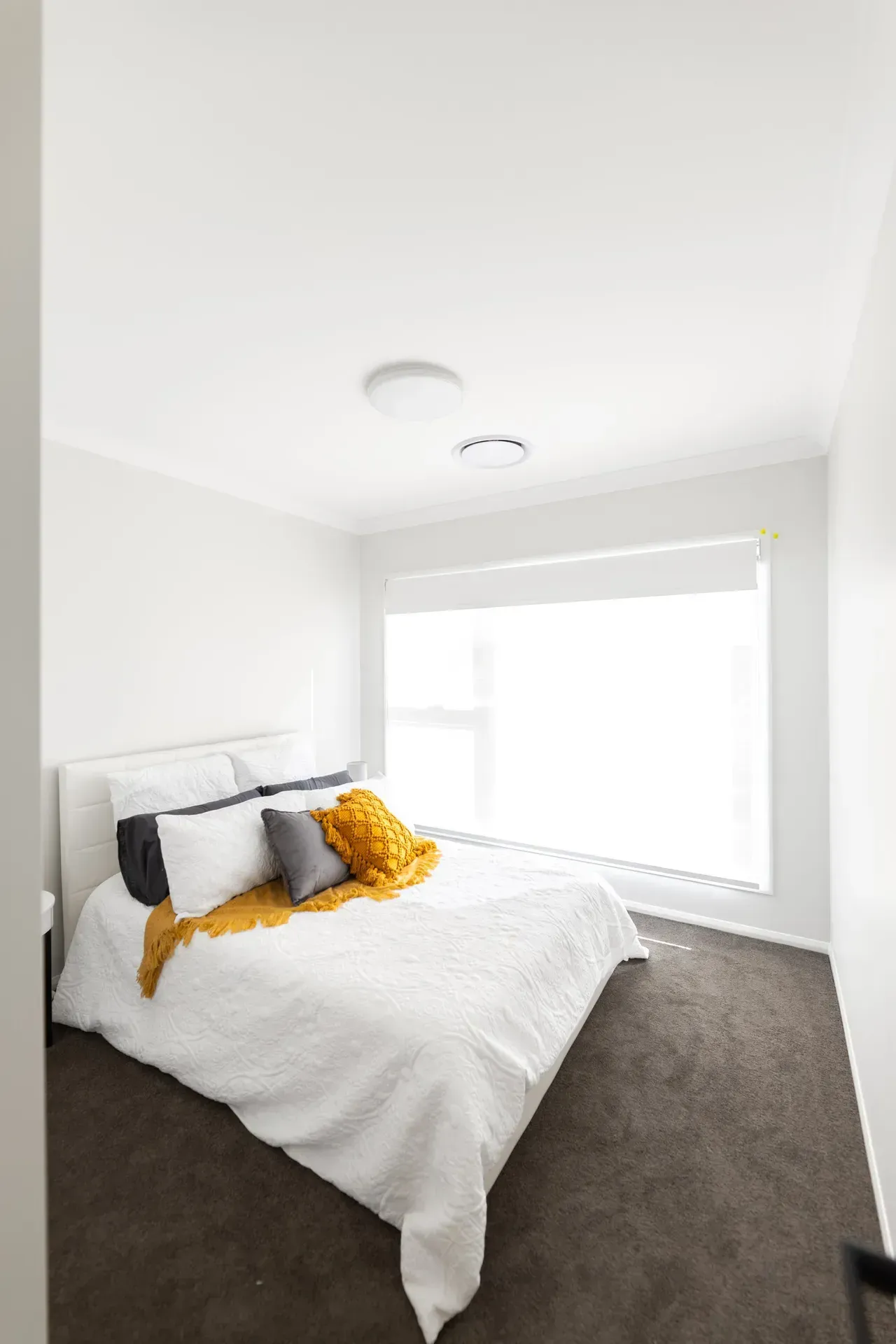 Bright bedroom with white bedding, dark pillows, and a large window with sheer blinds.
