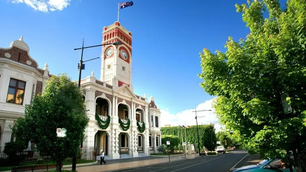 Historic civic building with clock tower, wreaths, and trees under a bright blue sky