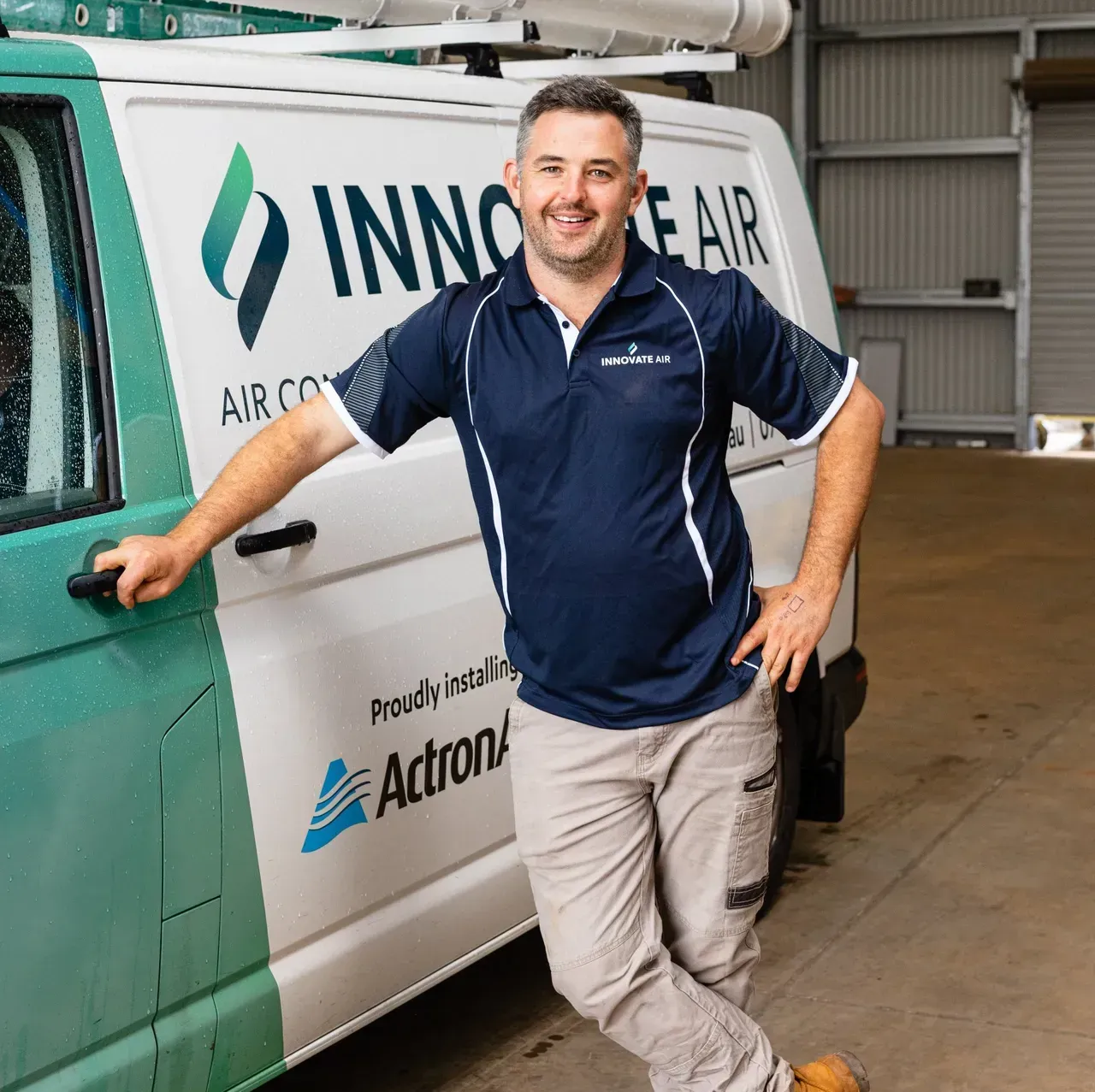 Smiling man leaning on a green and white branded service van in a garage.