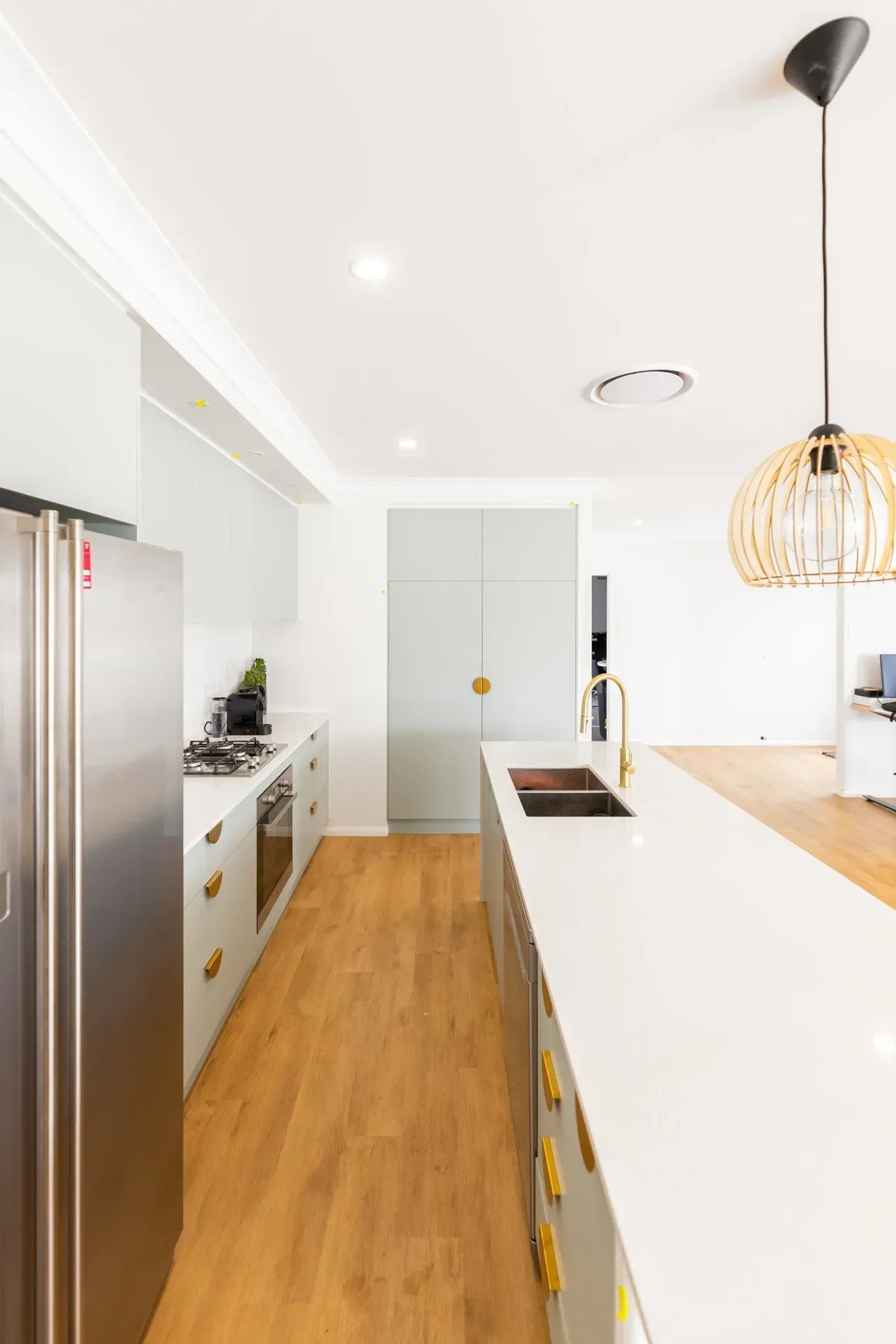 Bright modern kitchen with white cabinets, wood floor, stainless fridge, and a hanging pendant light