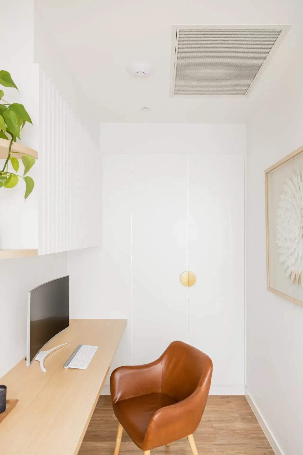 Minimalist white office nook with a wooden desk, tan chair, and closet doors