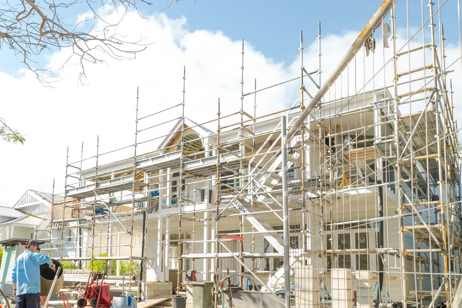 Scaffolding around a house under construction, with workers and building materials in bright sunlight