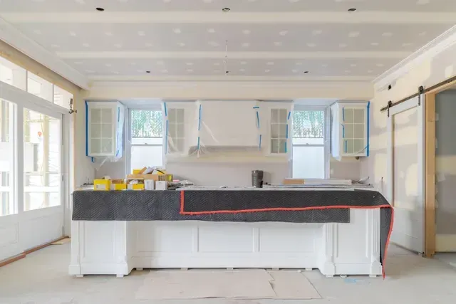 Bright kitchen renovation with white cabinets, dark countertop, and open windows around the island.