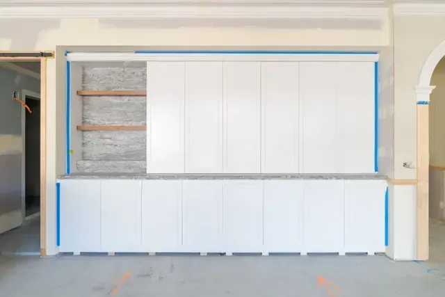 Built-in white cabinet wall with open shelving and blue tape outlines in a room under renovation