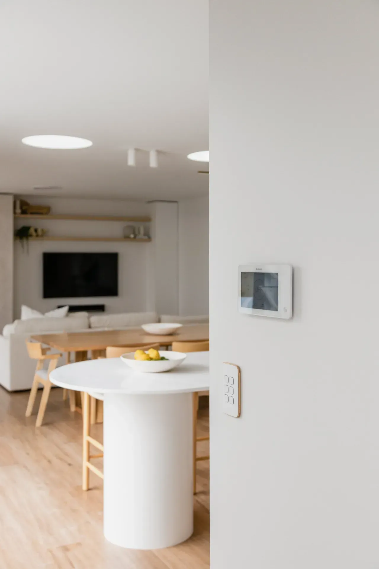 Bright modern dining-living room with white walls, wood floor, round table, sofa, and wall-mounted TV