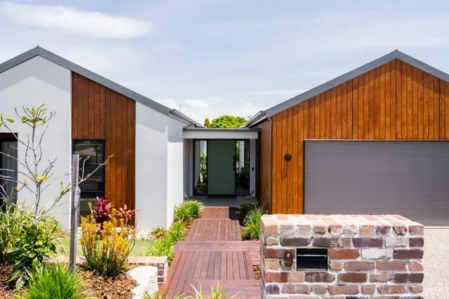 Modern house exterior with wood and white siding, front walkway, garage, and stone mailbox wall