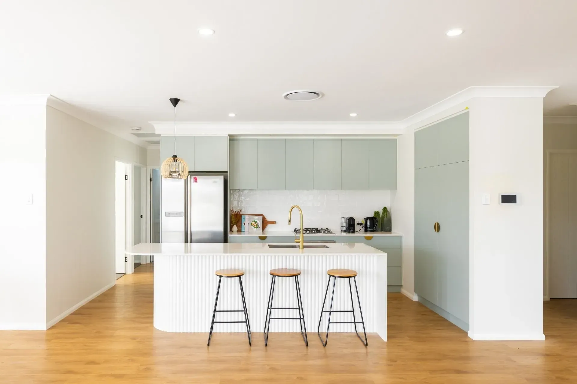 Bright modern kitchen with white island, black stools, brass accents, and light wood floors
