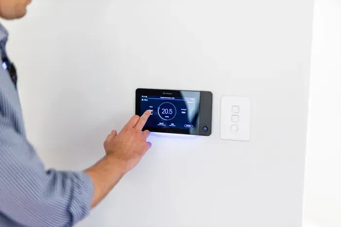 Person adjusting a wall-mounted smart thermostat with a touchscreen display