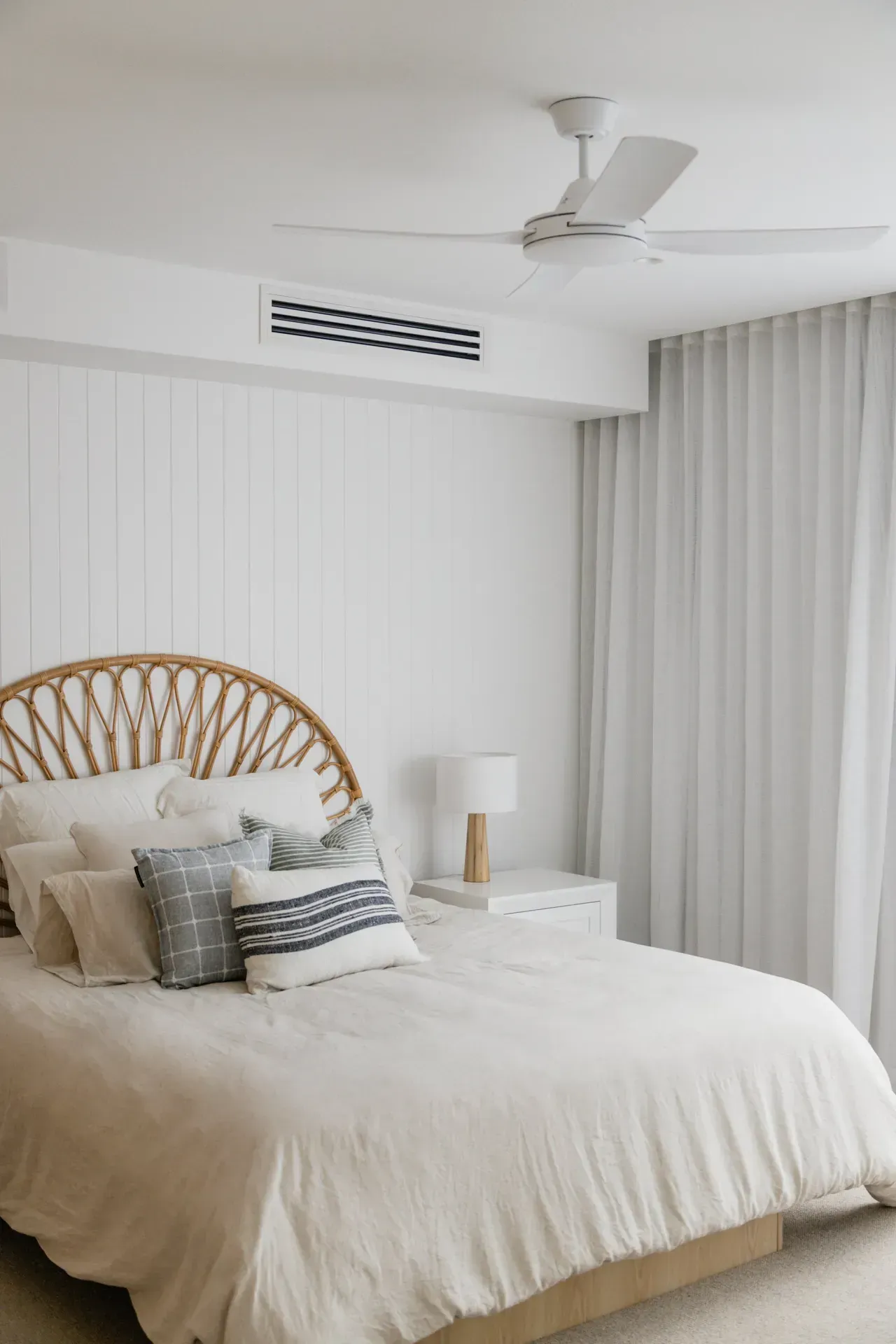 Bright bedroom with a wicker headboard, white bedding, and sheer curtains