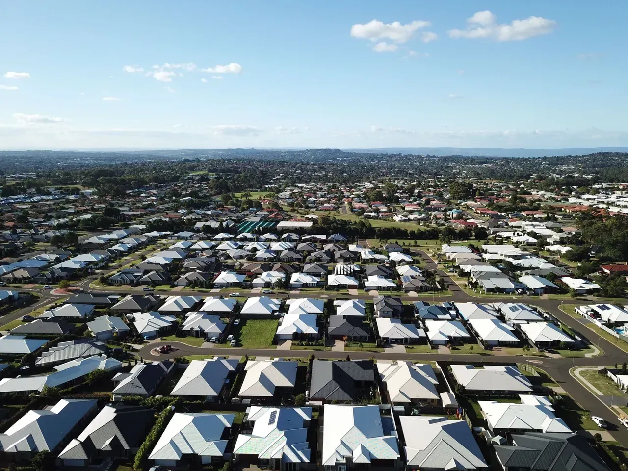 Aerial view of a suburban neighborhood with rows of white-roofed houses under a blue sky.