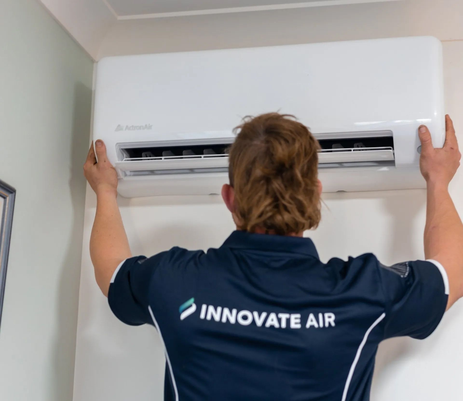 Technician installing a white wall-mounted air conditioner indoors