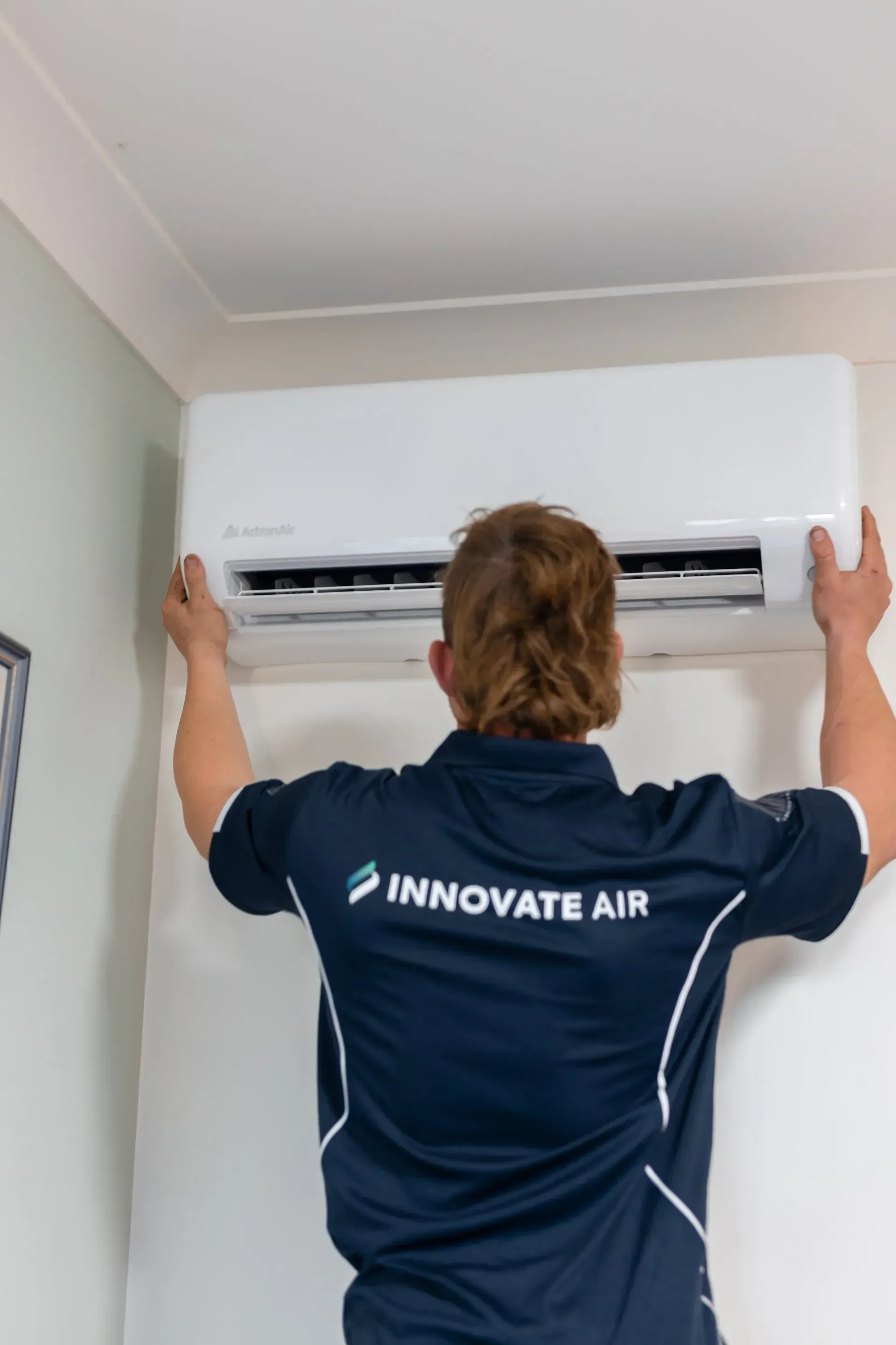 Technician installing a wall-mounted air conditioner in a white room