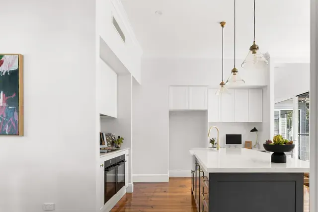 Bright modern kitchen with white cabinets, island, pendant lights, and wood floors