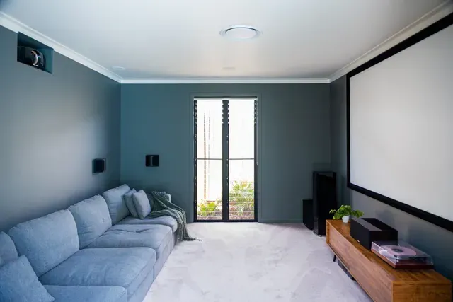 Modern living room with blue sectional sofa, large wall screen, and windowed door to a balcony