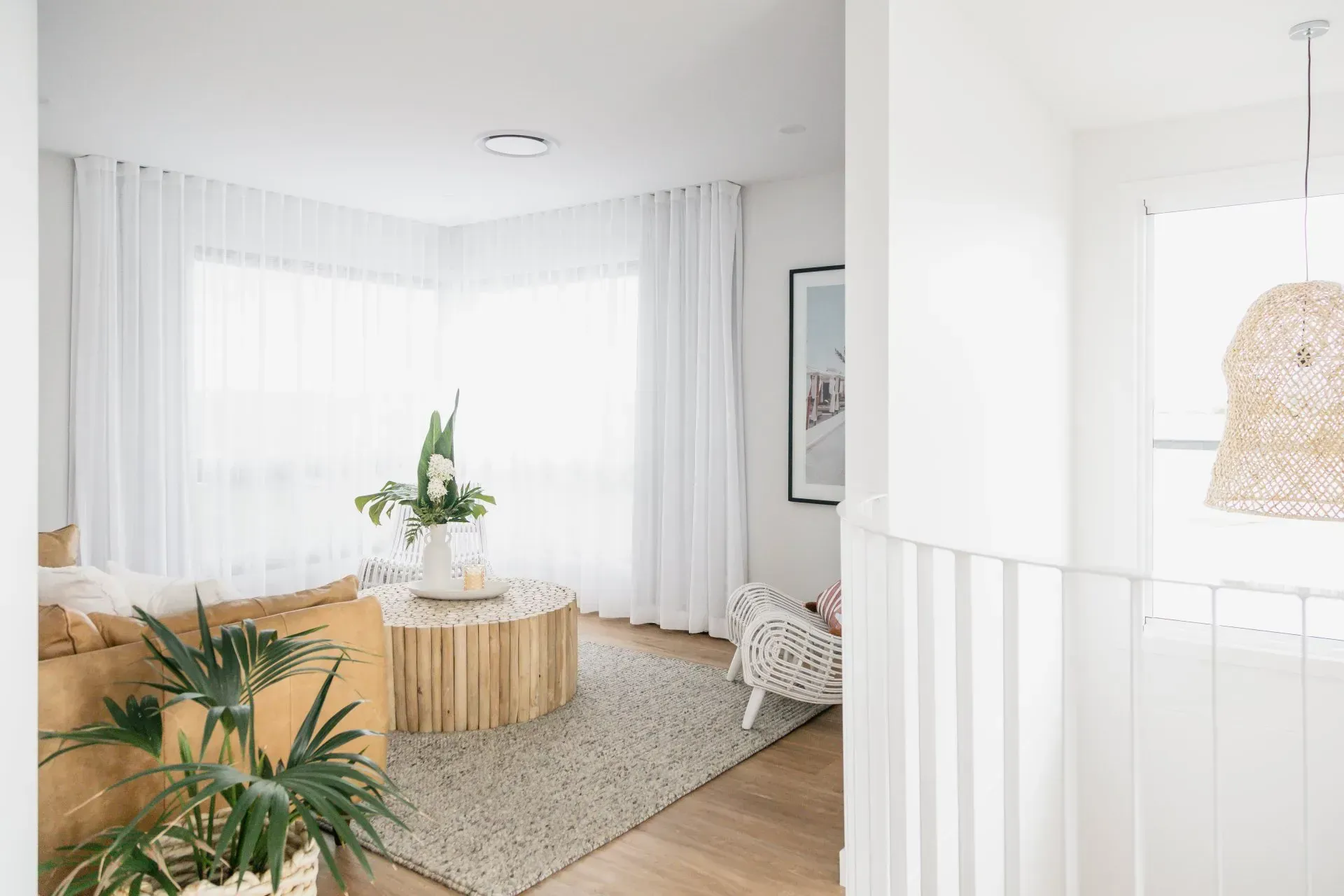 Bright white living room with large windows, woven coffee table, and green plants