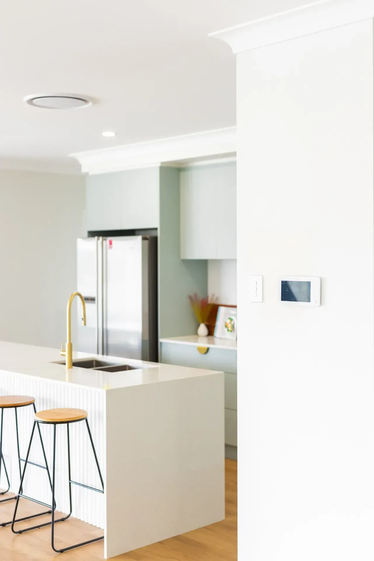Bright white kitchen with island, bar stools, stainless fridge, and gold faucet.