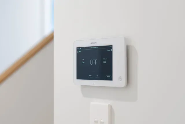 Wall-mounted white touchscreen thermostat on a beige wall near a staircase