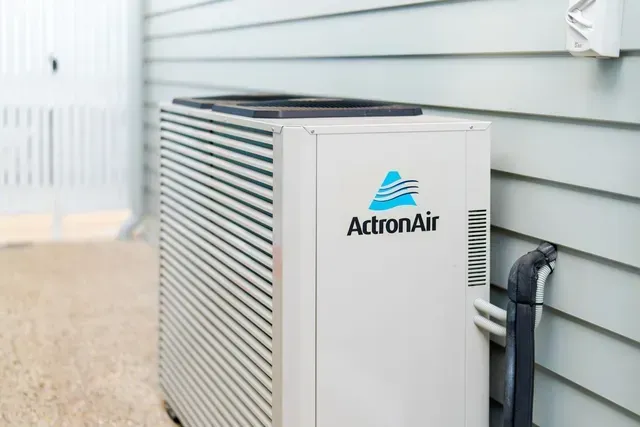 ActronAir outdoor air conditioner unit beside a house wall and fence