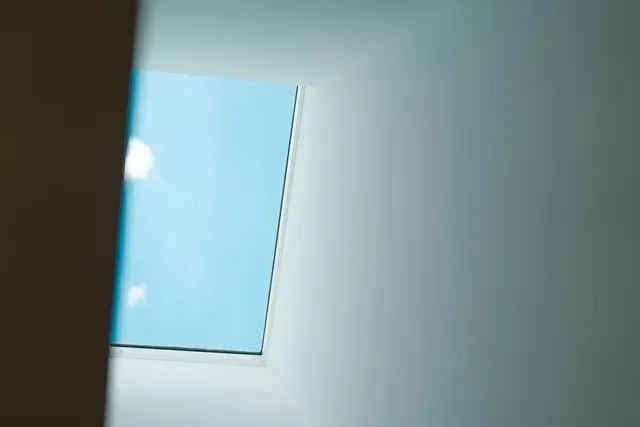 Partial view of a blue sky through a window against a white interior wall
