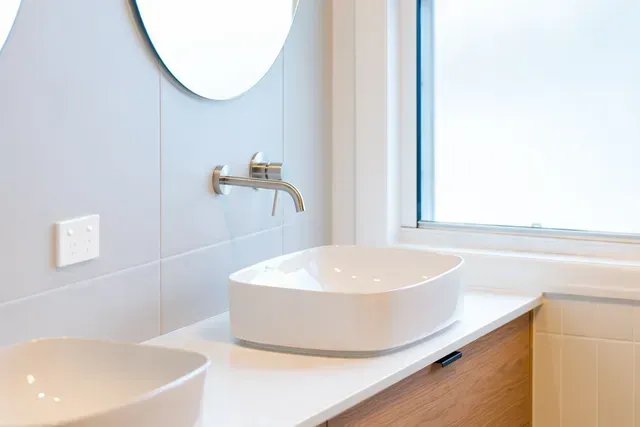 Modern bathroom vanity with white sink, mirror, and window-lit light blue walls