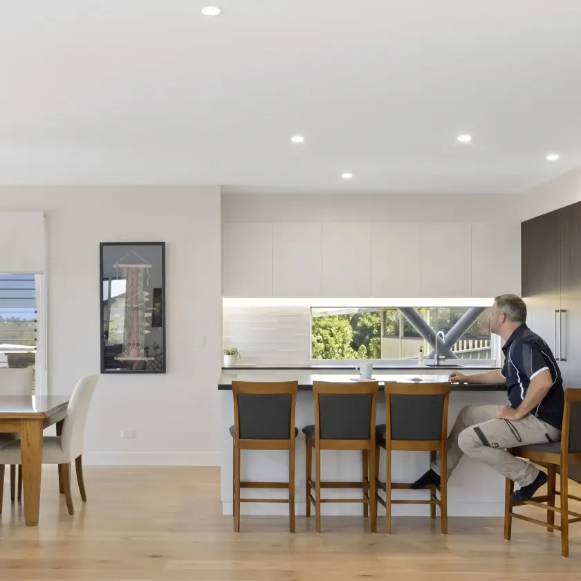 Bright modern kitchen with three wooden bar stools and a man seated at the island, looking out the window.