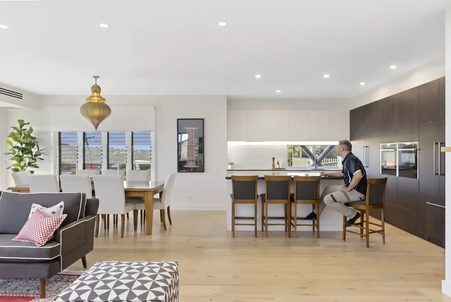 Modern open-plan kitchen and dining area with a person seated at the island and warm wood finishes.
